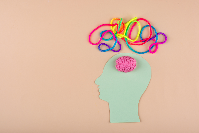 Neurodiversity at work concept showing a green head silhouette with a pink brain and colourful tangled threads, representing different thinking styles and cognitive diversity in the workplace.